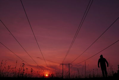 Silhouette man standing on electricity pylon against sky during sunset