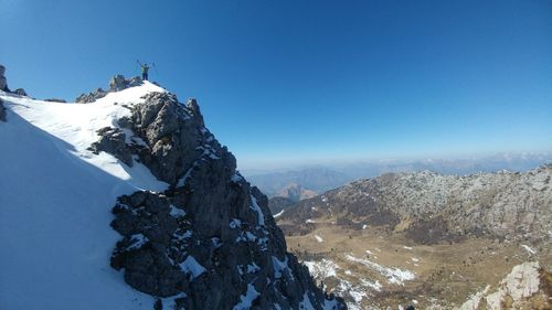 Distant view of woman standing on mountain against sky during winter