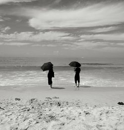 Rear view of people walking on beach against sky