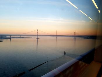 Suspension bridge over sea seen through glass against sky during sunset