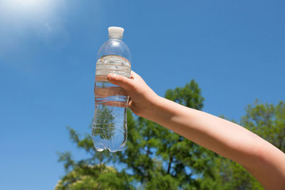 A child's hand is holding a bottle of drinking water against the blue sky
