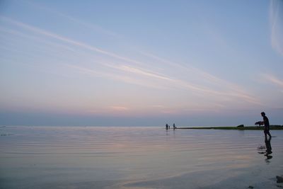 People standing on beach against sky during sunset