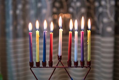 Hanukkah candlestick made of multi-colored candles, against the background of a curtained window.