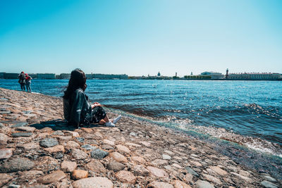 People sitting on rock by sea against clear sky