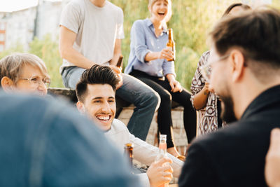 Male and female friends laughing while holding beer at garden party