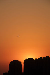 Silhouette airplane flying against orange sky