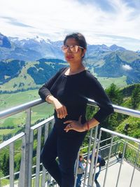 Portrait of smiling young woman standing on mountain against sky