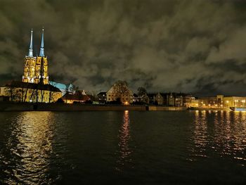 Illuminated buildings by river against sky at night