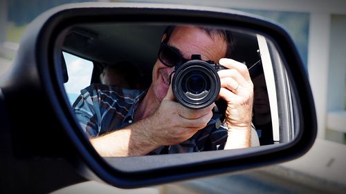 Reflection of man photographing on car side-view mirror