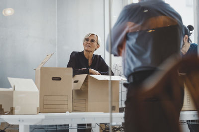 Mature businesswoman with moving boxes standing with colleagues in new office