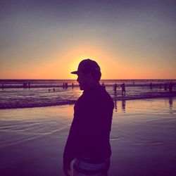 Rear view of man standing on beach against sky during sunset