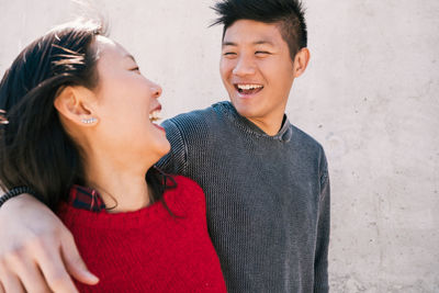 Laughing couple standing by wall outdoors