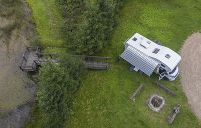 Aerial view of person sitting near camper van and wooden footbridge by lake