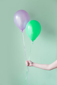 Cropped hand of person holding balloons against green background