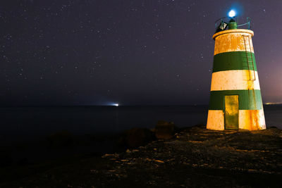 Lighthouse by sea against sky at night