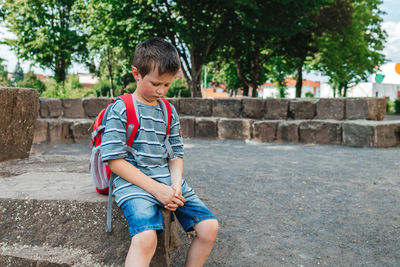 A sad schoolboy sits in the school yard with a backpack on his back. children's problems at school.