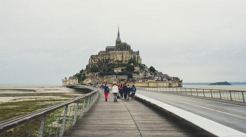 Rear view of people walking on bridge leading towards cathedral against sky