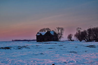 Building by frozen lake against sky during sunset