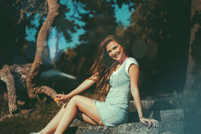 Young woman sitting by tree against plants