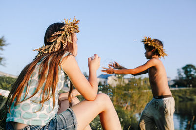 Cute girl blowing bubbles while standing with brother outdoors