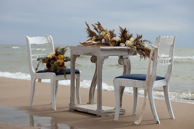 Chairs and table at beach by sea against sky