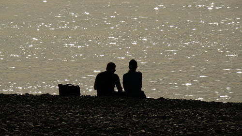 Silhouette couple sitting at beach during sunset