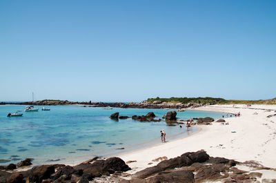 People on beach against clear blue sky