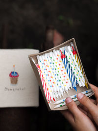 Child holding a paper box with colorful birthday candles on dark background.