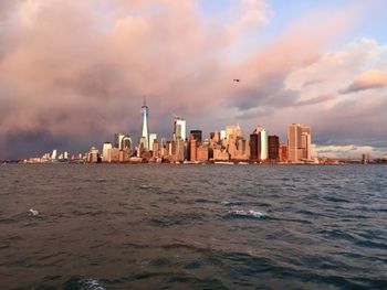 Sea by modern buildings against sky during sunset