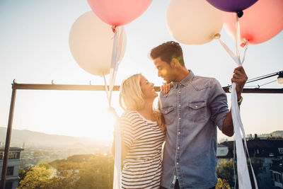 Couple standing with balloons against sky