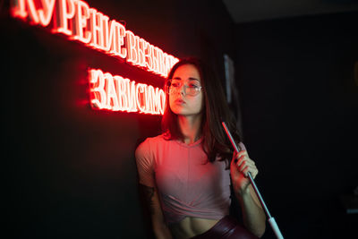 Young woman holding rod standing by illuminated sign