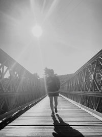 Rear view of man on footbridge against bright sun