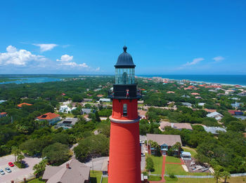 Lighthouse amidst buildings and sea against blue sky