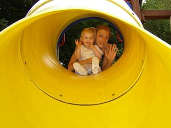 Portrait of happy mother with daughter in slide tunnel