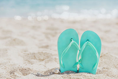 Turquoise, light blue flip flops or sandal shoe stuck in sand on sandy beach by sea coastline, ocean