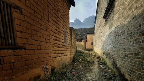 Alley amidst old houses by mountain against sky