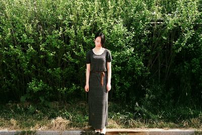 Full length of sad young woman standing against plants