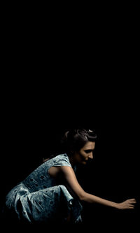 Side view of woman crouching against black background