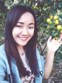 Portrait of smiling woman holding lemons on tree