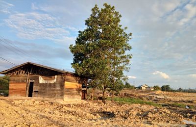 House on field by trees against sky