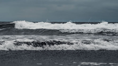 Waves rushing towards shore against sky