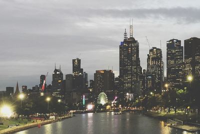 Illuminated buildings by river against sky in city