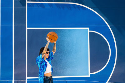 Caucasian girl with sunglasses and tattoos on a blue background with a basketball