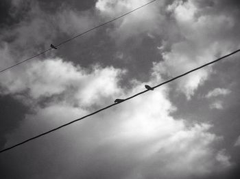 Low angle view of power lines against cloudy sky