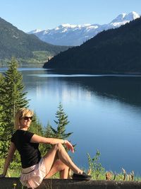 Portrait of woman sitting at lakeshore against mountains