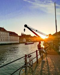 People riding bicycle on bridge over river in city at sunset