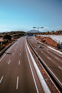 Diminishing perspective of highway against clear blue sky during sunny day