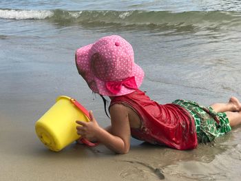 Girl holding bucket while lying at beach