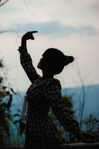 Young man with arms raised standing against sky