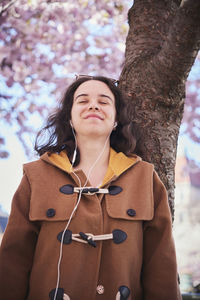 Young woman standing under cherry blossom and listening to music